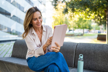 Mature businesswoman smiling using tablet outdoors in urban park