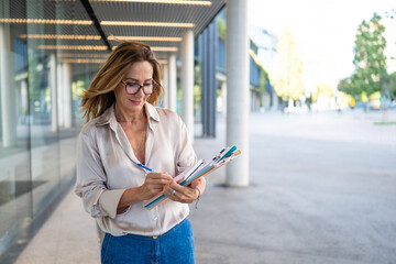 Mature businesswoman writing on clipboard in urban setting
