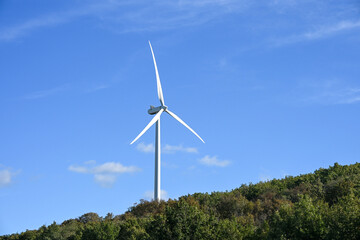 A modern white wind turbine rises above a green hillside against a clear blue sky, symbolising clean energy and sustainability