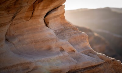 Close-up of layered sandstone cliff with holes and sunlight. Distant mountain views in bokeh