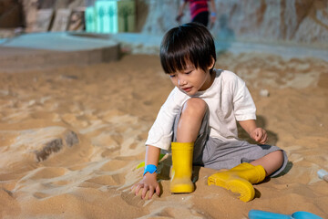 Kid happy face playing in the sandbox at the playground indoors. Cute boy plays with toys in the sand on the playground. Preschool creative activities and child development healthy.