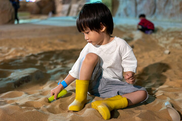 Kid happy face playing in the sandbox at the playground indoors. Cute boy plays with toys in the sand on the playground. Preschool creative activities and child development healthy.