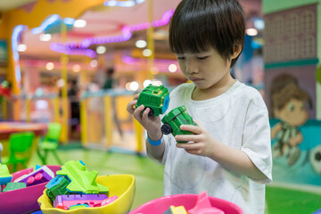 Kid happy face playing with plastic bricks. Child play with blocks plastic in indoor playground. Cute boy playing toy colorful blocks. Preschool activities and early childhood education.