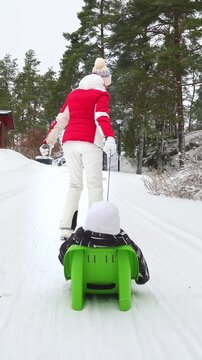 Grandmother pulling child on sled in snowy Finland, enjoying winter family lifestyle outdoors. Warm clothing, joy, love, and seasonal holiday atmosphere in bright daylight.