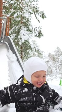 Happy child in warm winter clothes sliding down a snowy slide outdoors, smiling with joy. Fun seasonal lifestyle, healthy activity, bright light and fresh frosty air.