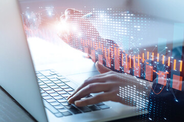 Hands on laptop keyboard with pen nearby and digital business graphs overlay.