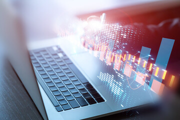 Hands using laptop with pen lying on notebook, futuristic financial charts overlay.