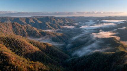 Breathtaking aerial view of a layered mountain range at sunrise, showcasing autumn colors and misty fog, captured in golden hour light.