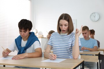 Students taking exam at wooden table indoors