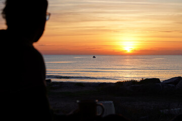 nomadic life. sunrise on the beach and person watching it, out of focus in the foreground