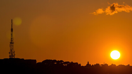 Fototapeta premium Rome at sunset timelapse with the fiery orb of the sun dropping below the horizon above the rooftops of the historical buildings