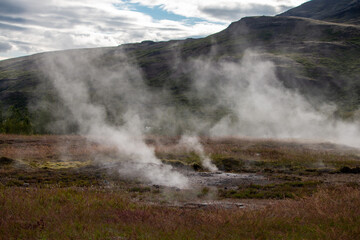Steaming Geothermal Landscape with Lush Hills Under a Cloudy Sky in a Volcanic Region