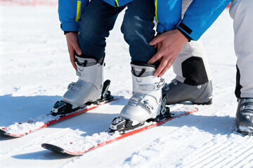 Close-up of child learning to ski with adult guidance on snowy slope