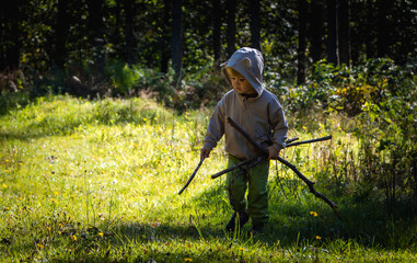 Little boy plays with sticks while walking in the forest