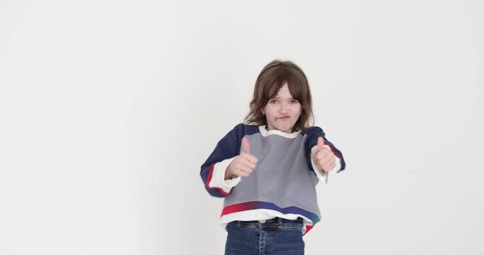 Preteen schoolgirl jumps with excitement and shows thumbs-up with tiny hands against white background. Child expresses happiness. Slow motion