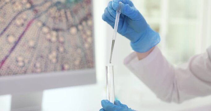 Scientist drips clear solution with pipette into test tube in bright lab. Researcher tracks reaction on bench recording values in notebook slow motion