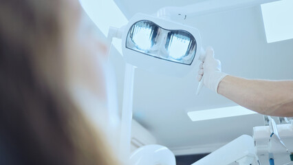 A dental professional, wearing gloves, holds a bright dental light, illuminating a patient's mouth...
