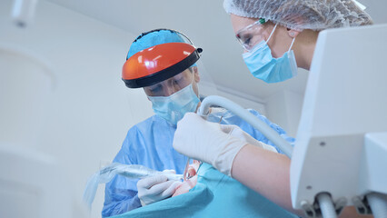 In a sterile dental clinic, a dentist and assistant, both in protective gear, meticulously perform...