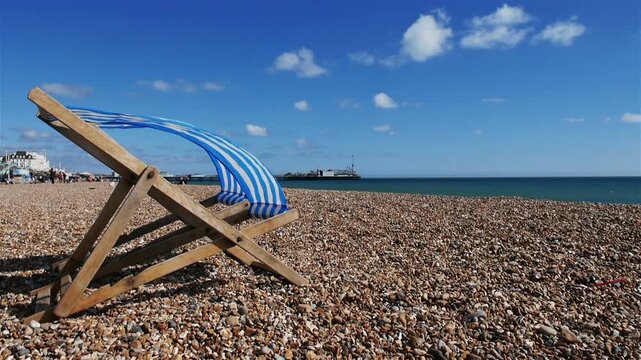Deckchairs on Brighton Beach. A view of an empty and blustery pebble beach at Brighton on the south coast of England with the iconic pier visible in the distance.