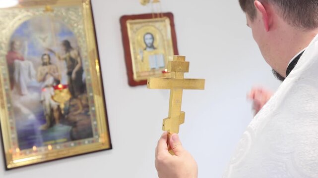 Priest Holding Cross Praying in Front of Religious Icon During Sacred Moment Inside Church