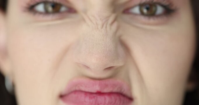 Funny young woman scrunches up face grimacing in bright light. Playful actress warms up facial muscles before stage performance at rehearsal in studio