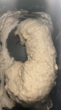Top-down view of a bread maker mixing dough during the kneading process. Homemade bread preparation, rotating blades. Concept of home baking.