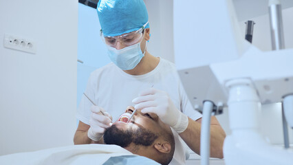 A dentist in protective gear examines a patient's mouth in a clinical setting, highlighting dental...