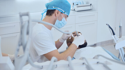 A dentist in protective gear examines a patient's mouth in a clean, organized clinic, emphasizing dental health and professional care.