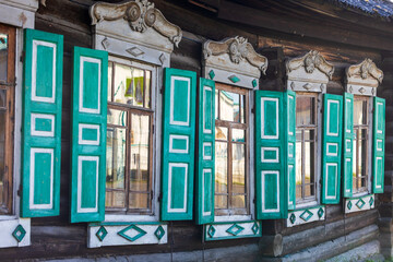 Row of windows on ground floor with carved frames and turquoise and white open shutters on old wooden logs house, Russia. Close-up of historic facade of an old village house