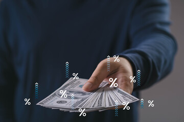 Hand offering spread of US dollar bills with percentage signs, symbolizing interest rates,...