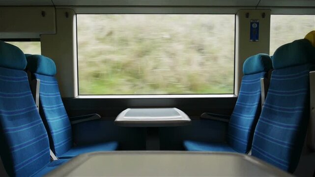 British Train Journey. A symmetrical view across an empty UK train carriage with a view out of the window looking at the passing countryside.