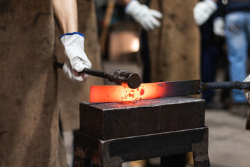 Group of craftsman is forging iron tool in workshop