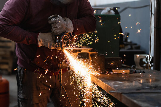 Man working with rotary angle grinder at workshop, closeup detail, orange sparks flying around