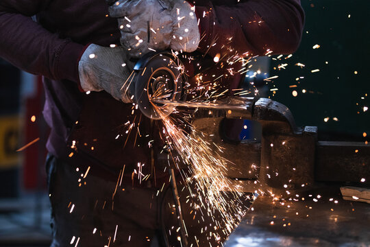 A close-up of a car mechanic using a metal grinder to cut a car bearing in an auto repair shop, bright flashes flying in different directions, in the background tools for an auto repair