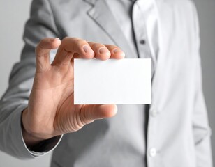 Person's Hand Presenting Blank Business Card in a Gray Suit Against Soft Gray Background