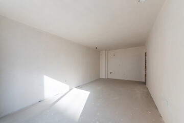 Interior of an empty room under construction in a new apartment. Unfinished space with raw concrete walls, floor, and a large window. Renovation and real estate concept.
