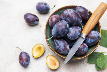 Fresh plums in bowl with knife on gray background