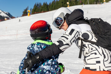 Mother teaching child to ski on sunny mountain slope, holding and guiding for balance and...