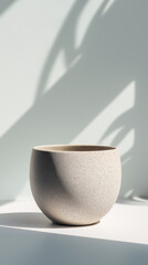 Empty ceramic planter with a textured surface in bright natural light. Minimalist home decor with soft plant shadows on a neutral background