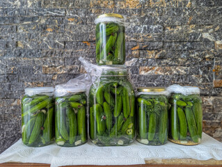 Homemade Pickled Cucumbers in Glass Jars on Stone Wall Background