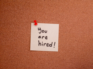 Handwritten you are hired note pinned on cork bulletin board