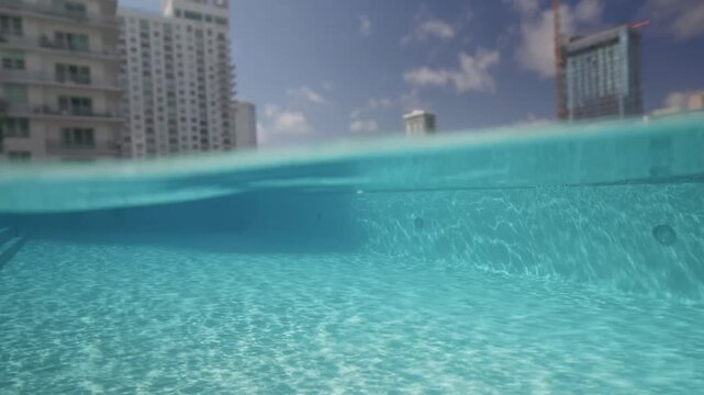 Slow motion video of a young tourist man jumping into a pool at sunrise in Miami, Florida. Split-level shot showing him above and below the water with sunrays on the surface