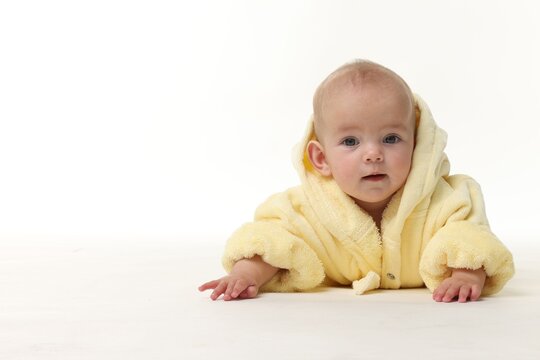 Fototapeta Cute baby in bathrobe crawling on white background. Space for text