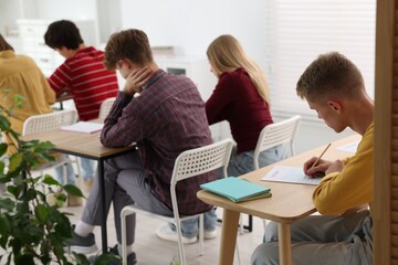 Students taking exam at wooden table indoors, selective focus