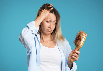 Alopecia problem. Sad woman holding brush with lost hair on light blue background