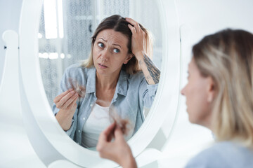 Alopecia problem. Worried woman with clump of lost hair near mirror at home