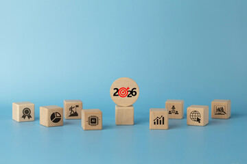 Wooden blocks featuring a round 2026 target icon and business symbols AI, analytics, growth, teamwork, global on a blue background, illustrating business planning, strategy, KPI and goals for 2026