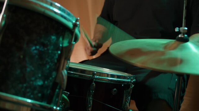 Drummer playing on concert, close up in studio, drummer hands hit the drum cymbal with drumstick in a dark studio. Drummer plays the drums in the recording studio. Music band rehearsal