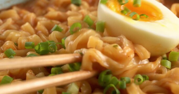 Korean spicy ramyeon noodle soup, with egg and green onion. Chopsticks pick up noodles.