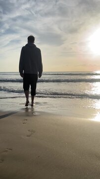 A person is standing on the beach with their hand in the air. The sky is cloudy and the sun is setting